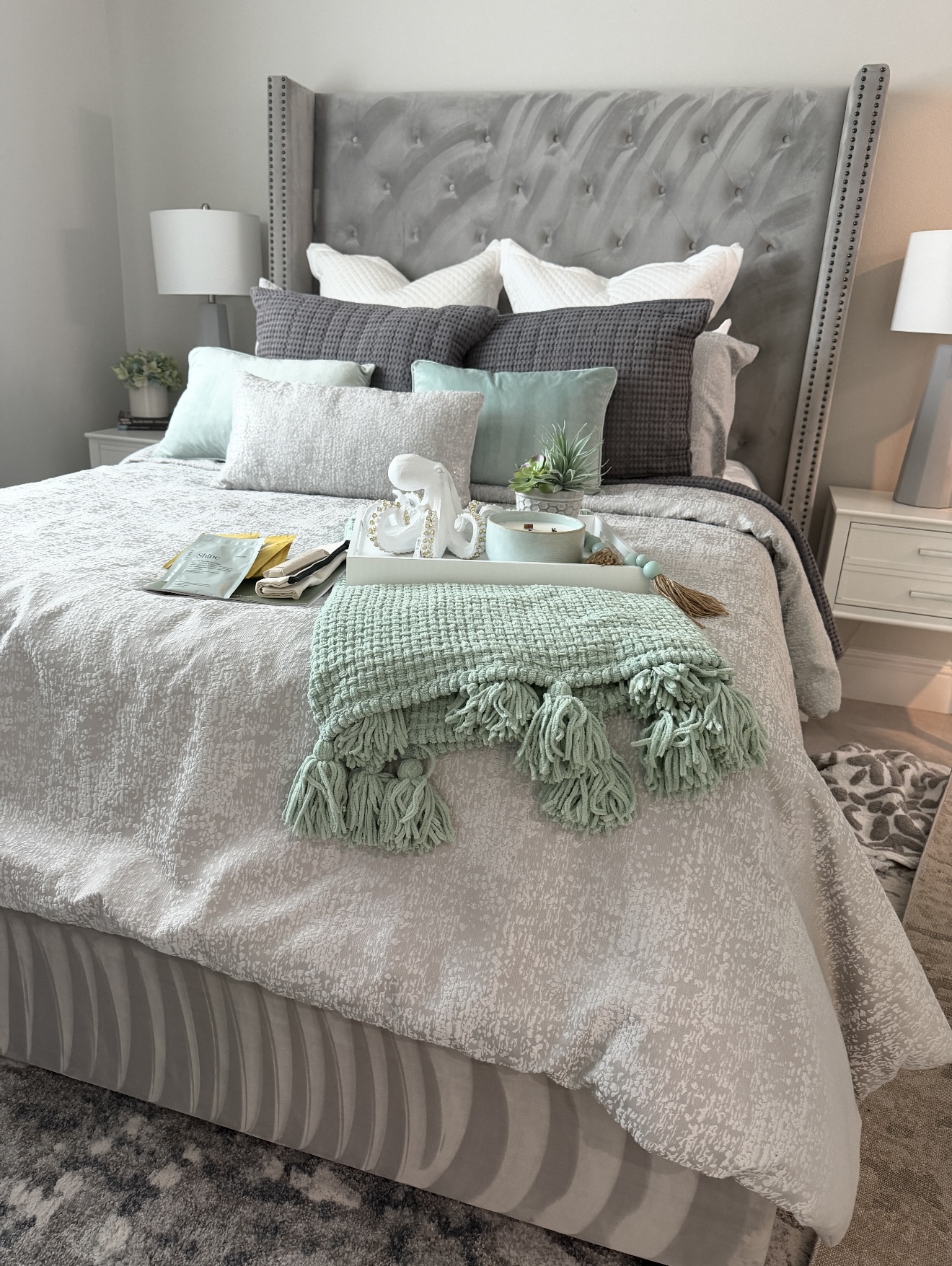 A made bed with mint bedding, a decorative tray and a folded towel figure