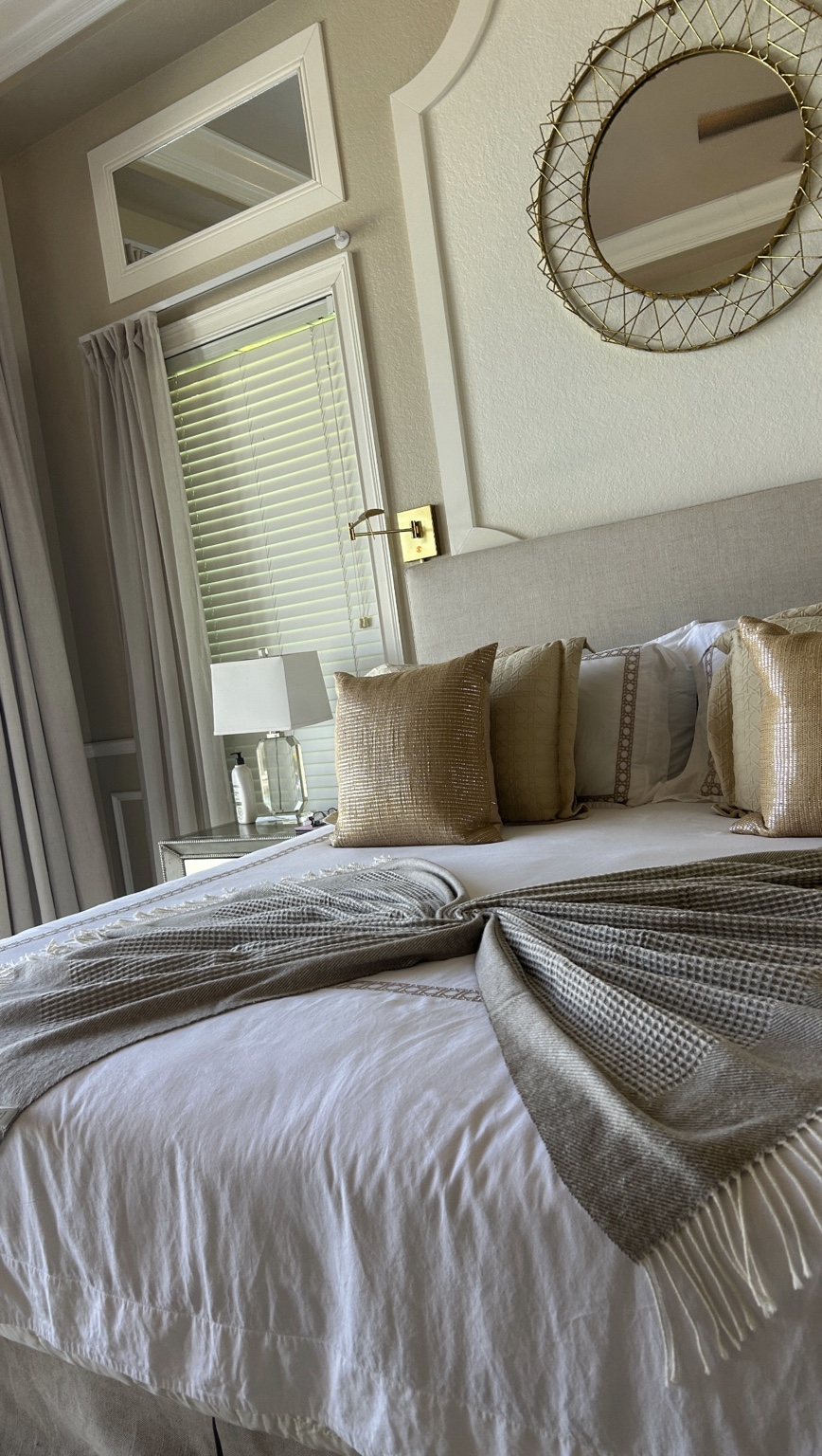A freshly made bed with gold pillows and a gray throw arranged in a fan shape